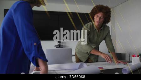 Pointing, man in green shirt leaning over plans at conference table with colleague in blue blouse Stock Photo