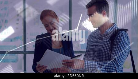 Reviewing two colleagues examining papers near glass windows, navy blazer and checked shirt, chart Stock Photo