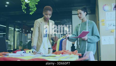 Two women designers examining fabrics in studio, in blazer and sweater holding measuring tape Stock Photo