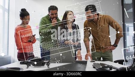 Reviewing team of six inspecting table in office, wearing jackets, with drone, laptop and overlays Stock Photo