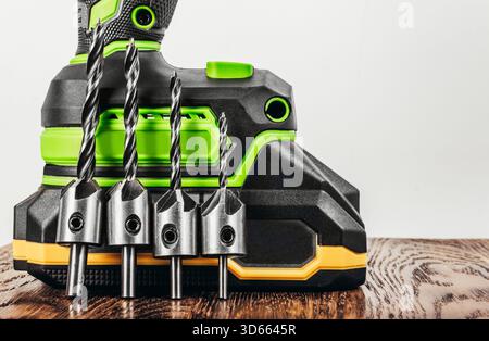 Photo of cordless green colored screwdriver with lithium accumulator battery on wooden surface with drill bits set. Stock Photo