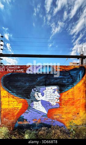 Colorful mural of a man in a hat with a vivid orange background painted on a brick wall under a bright blue sky with scattered clouds Stock Photo