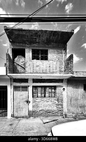 Black and white image of a modest unfinished brick house with exposed concrete and metal door in a residential urban area Stock Photo