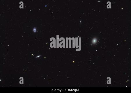 Eighth magnitude Messier galaxy M49 in Virgo, a bright elliptical galaxy. It was discovered by Charles Messier in 1771. It is accompanied by two bright galaxies to the left (east), the 10th magnitude face-on spiral NGC 4535 at top left and the 9th magnitude edge-on spiral NGC 4560 at bottom left. Together they form a trio of three different and distinct galaxy types and morphologies. Many other faint galaxies from the NGC, UGC and PGC catalogues populate the field. Stock Photo