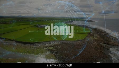 Hovering mesh globe projecting orbital rings over coastal fields and rocky shore, showing farms Stock Photo