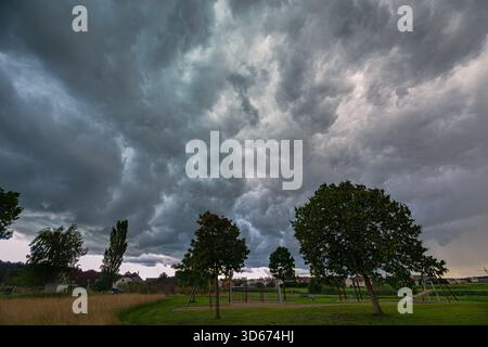 Dramatic stormfront clouds sweeping over the Bavarian countryside in Germany with dark trees in the foreground Stock Photo