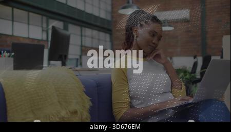 Working woman wearing yellow-sleeved white shirt using laptop on blue sofa in office, copy space Stock Photo