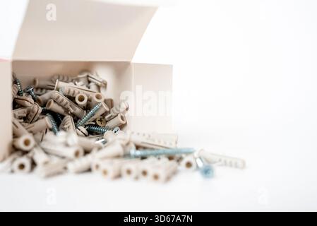 Assorted screws and wall plugs scattered from an open box on a white background. Building materials and home renovation concept. High quality photo Stock Photo