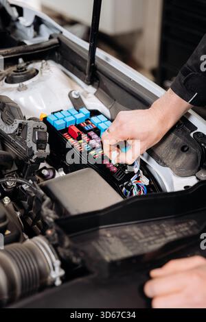 Mechanic replacing car fuse in engine bay fuse box, auto service maintenance close up Stock Photo