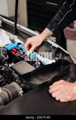 Mechanic replacing car fuse in engine bay fuse box, auto service maintenance close up Stock Photo
