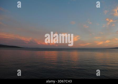 Theatrical play of wind and clouds in many tones of blue, pink, red, orange illuminated of sunset light with reflections on the peaceful Adriatic sea Stock Photo