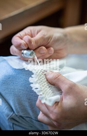 Experienced hands carefully create smocking on white fabric with needle and thimble Stock Photo