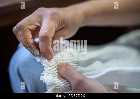 Hands creating smocking stitches on white fabric using a needle, thread, and thimble Stock Photo