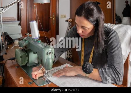 Woman focusing on sewing garment with fabric at her home studio Stock Photo