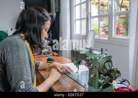Woman focusing on fabric under the needle of an old sewing machine Stock Photo