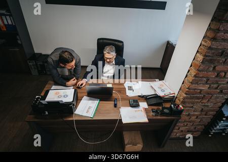Two professionals collaborating in an office, discussing charts and data at a desk Stock Photo