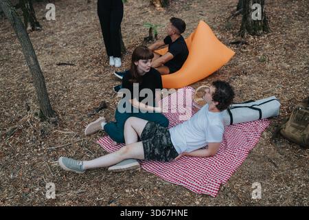 Friends relaxing in a park picnic setting, chatting on a checkered blanket and camping gear Stock Photo