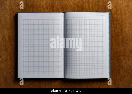 Open notebook with checkered sheets on wooden texture background, close up, top view, copy space Stock Photo
