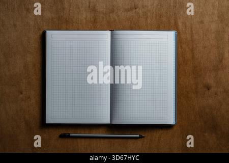 Open notebook with checkered sheets and pencil on wooden texture background, close up, top view, copy space Stock Photo