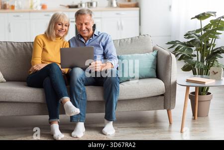 Cheerful Senior Spouses Using Laptop Watching Movie Online At Home Stock Photo