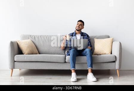 Man using pc sitting on the couch, drinking coffee Stock Photo