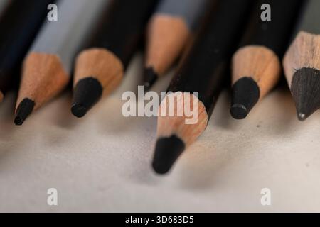 a row of black wooden pencils folded on cheap loose paper, wooden pencils with graphite lead for drawing or other work Stock Photo