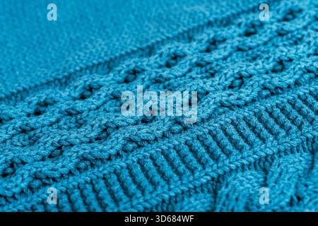 Closeup of teal knitted wool fabric with visible braided lines, thick interlocked stitches and soft textured yarn forming a warm cozy textile surface. Stock Photo