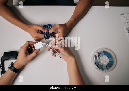 High-angle view of two technicians connecting RGB led strip lights using remote control and controller, adjusting backlight settings for customized Stock Photo