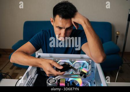 Portrait of puzzled technician upgrading desktop computer by installing wi-fi module, focusing intently on task with thoughtful expression, showcasing Stock Photo