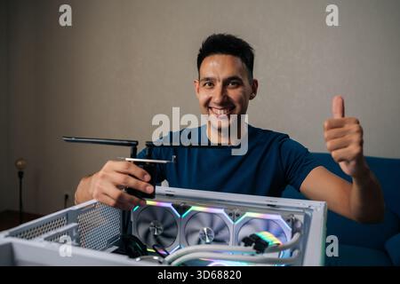 Cheerful computer technician smiling looking camera during installing wi-fi module into custom-built desktop computer with RGB lighting, showing Stock Photo