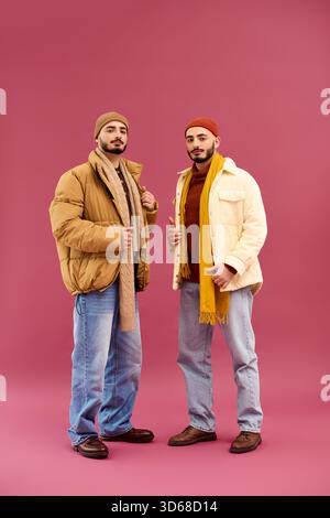 Two handsome twin brothers pose confidently in stylish winter attire against a bright backdrop. Stock Photo