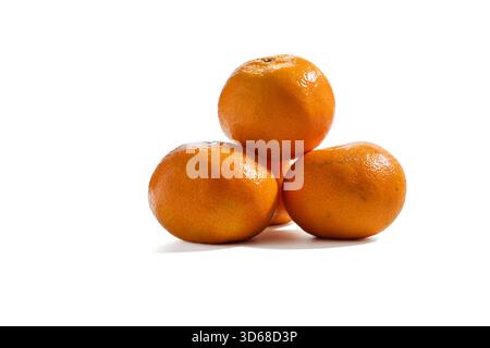 Three mandarin oranges Citrus reticulata stacked in a small pyramid on white. The bright, textured peel suggests freshness and natural sweetness. Stock Photo