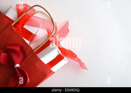 Detail of concept of giving gifts at an event celebration with a red paper shopping bag with ribbon filled with white gift boxes with red on white tab Stock Photo