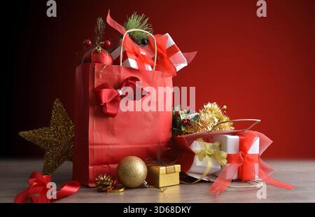 Concept of giving gifts at Christmas with red gift bags full of gift packages and Christmas decorations on a wooden table and red gradient background. Stock Photo