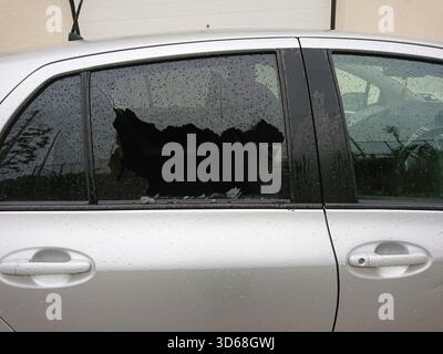 Car break-in with shattered smashed side window. Economic downturn fuels street criminality, shattered vehicle glass signaling hardship and criminalit Stock Photo