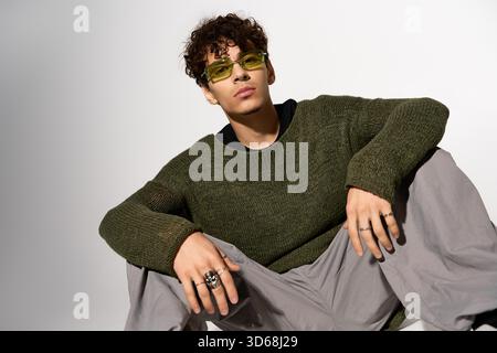 A trendy young man with curly hair and sunglasses relaxes in a studio. Stock Photo