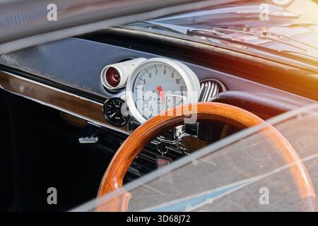Close view of vintage car dashboard with wooden steering wheel, large analog tachometer and chrome details, warm sunlight flare Stock Photo