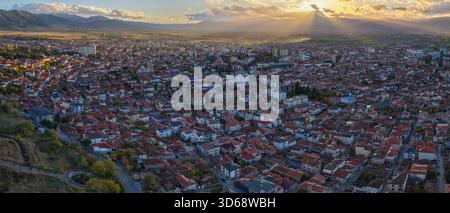 Dramatic sunset panorama over Korçë with golden sun rays streaming through clouds and illuminating the city and surrounding valley. Stock Photo