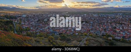 Dramatic sunset panorama over Korçë with golden sun rays streaming through clouds and illuminating the city and surrounding valley. Stock Photo