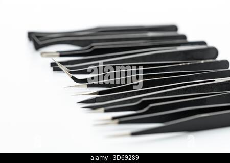 A set of various black precision tweezers with different angled and straight steel tips arranged closely on a white surface, showcasing a range of fin Stock Photo