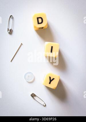 vertical diy sewing concept with needle safety pins and button on minimalist white background Stock Photo