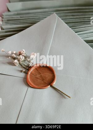Close-up of a rustic bronze wax seal and dried baby's breath flowers on a stack of light green envelopes Stock Photo