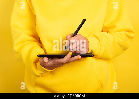 Person in yellow sweater using digital drawing tablet and stylus. Modern creative workspace with monochrome color scheme, ideal for tech and design th Stock Photo