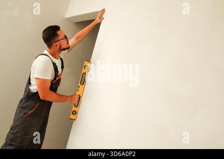 A uniformed worker uses a spirit level, bubble level, against a freshly built wall of a new building. business construction quality control wall level Stock Photo