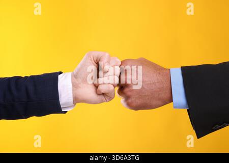 African American man bumping fists with his business partner on yellow background, closeup Stock Photo