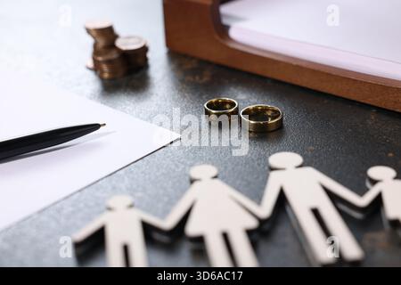 Alimony. Figures of family, wedding rings, pen, documents and coins on dark table, closeup Stock Photo