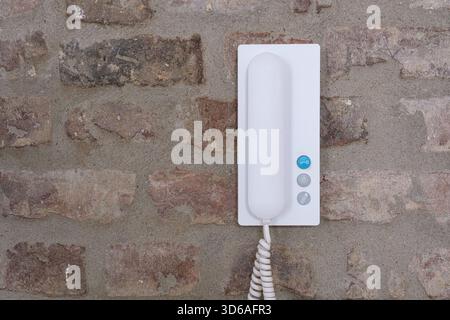 White wall-mounted intercom phone on a rustic brick wall Stock Photo