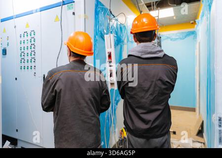 Two construction workers in hard hats inspecting electrical panels at building site Stock Photo