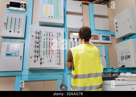 Technician checking control panels with indicator lights in industrial control room Stock Photo