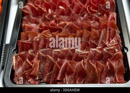 A close-up view of a deliciously arranged platter of thinly sliced cured meat. perfect for culinary presentations, this savory selection is ideal for Stock Photo